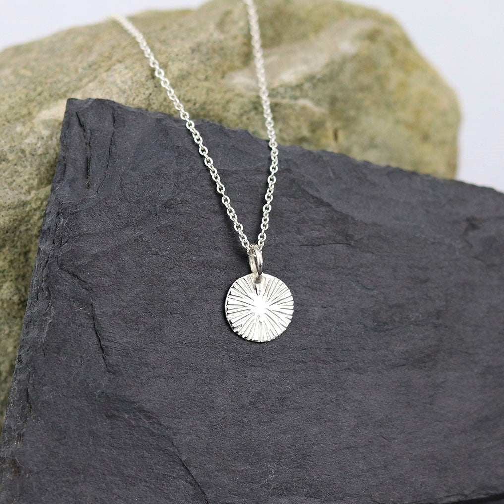 Collier médaille mini soleil en argent pour femme, posé sur une ardoise naturelle