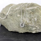 Collier médaille mini soleil en argent pour femme, posé sur une pierre grise