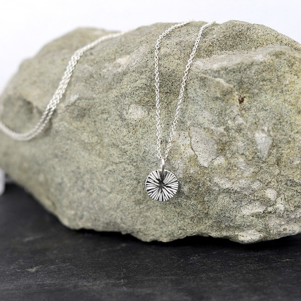 Collier médaille mini soleil en argent pour femme, posé sur une pierre grise