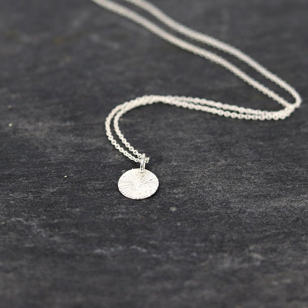 Collier médaille mini soleil en argent pour femme, posé sur une ardoise naturelle
