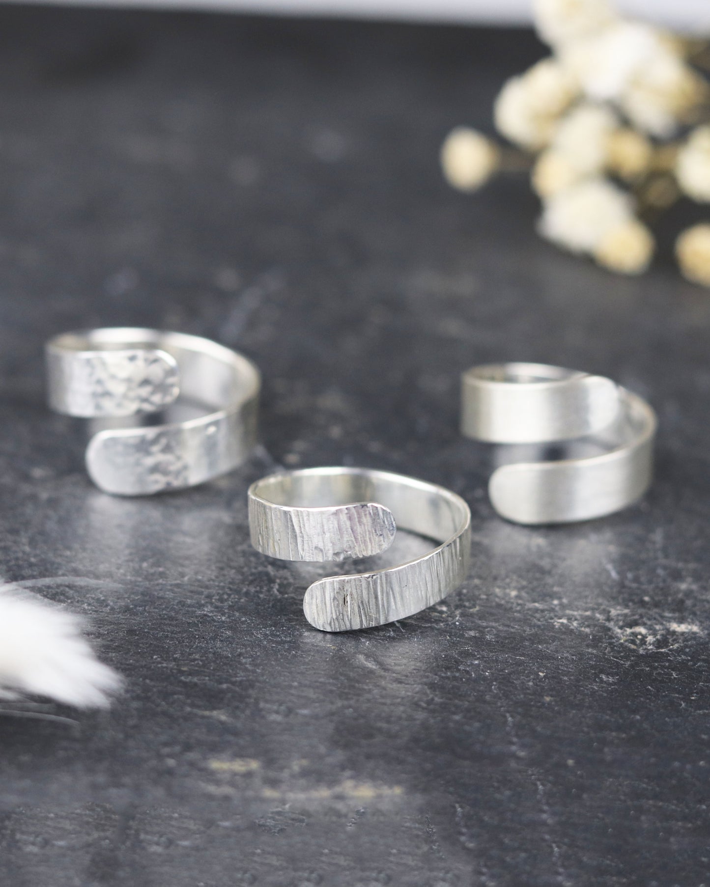 Bague Marion Chappaz réglable Ruban Twist en argent finition ciselée posée sur fond ardoise avec les finitions martelées et brossées posées à coté