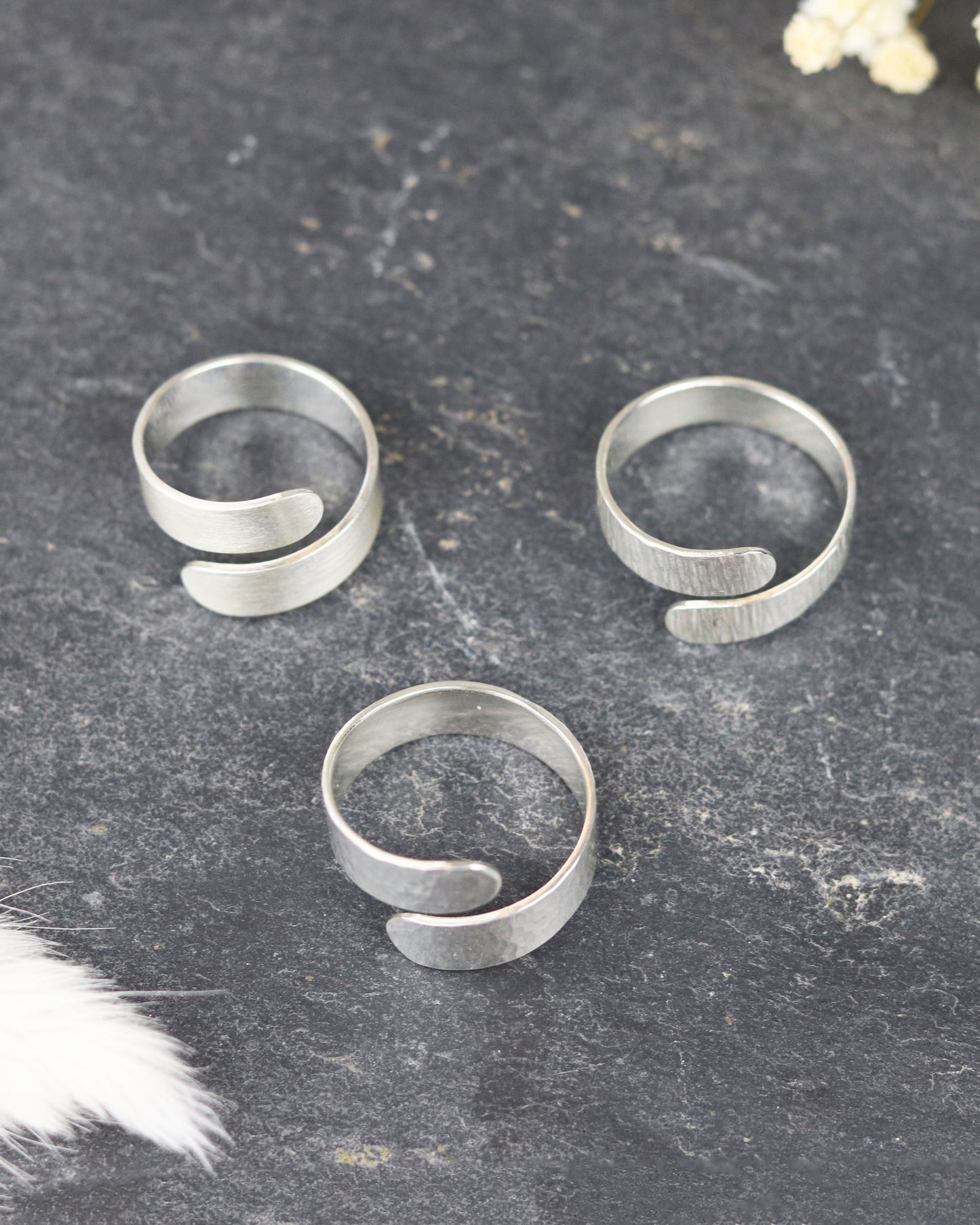 Bague Marion Chappaz réglable Ruban Twist en argent finition ciselée posée sur fond ardoise avec les finitions martelées et brossées posées à coté, vues de dessus