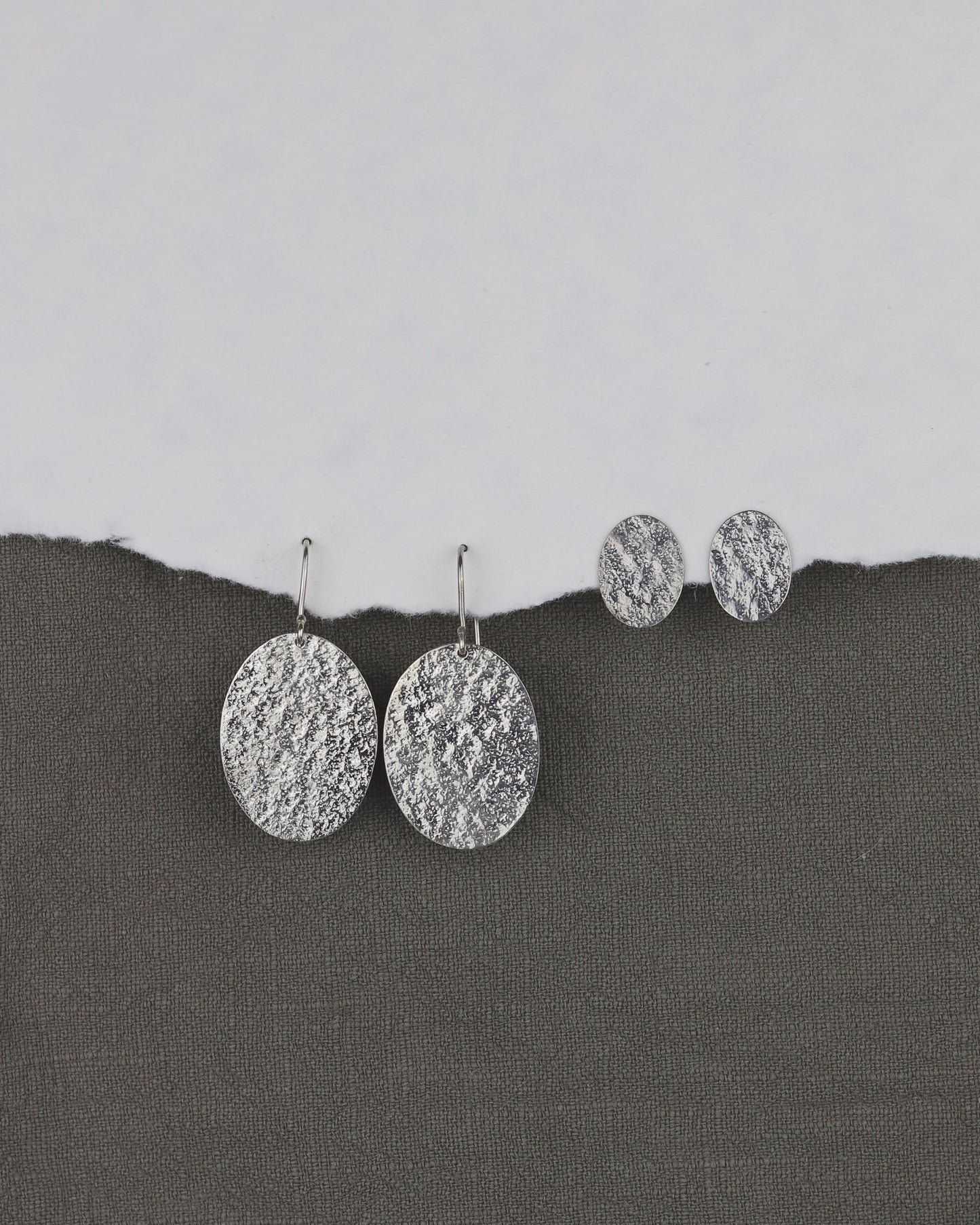 bijoux marion chappaz en argent 925 boucles d'oreilles Emery texturées puces fermoir poussoir papillon tirette belge sur papier blanc et fond tissu kaki pour femme avec les pendantes emery