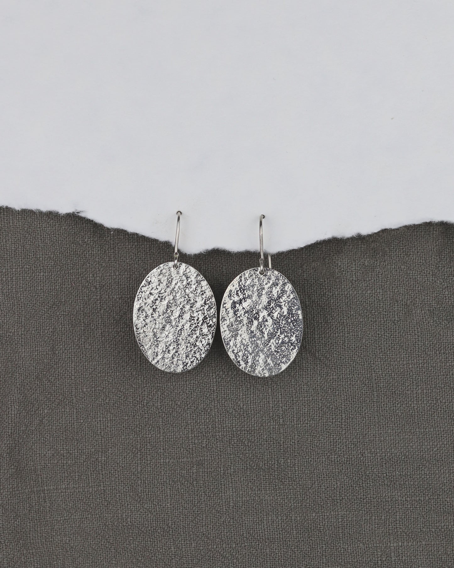 bijoux marion chappaz en argent 925 boucles d'oreilles texturées dormeuses ovales pendantes Emery pour femme sur fond tissu