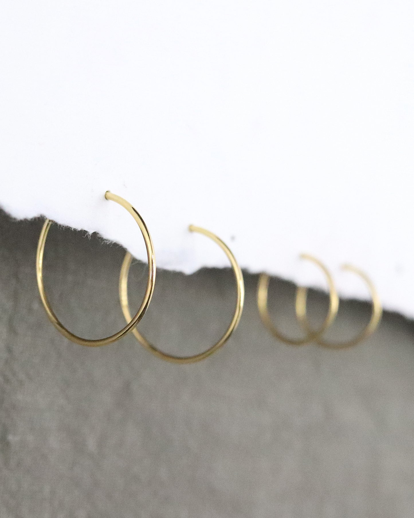 Boucles d'oreilles Créoles en or jaune 750 millièmes lisses fines sur un support en papier blanc et fond vert kaki Marion Chappaz