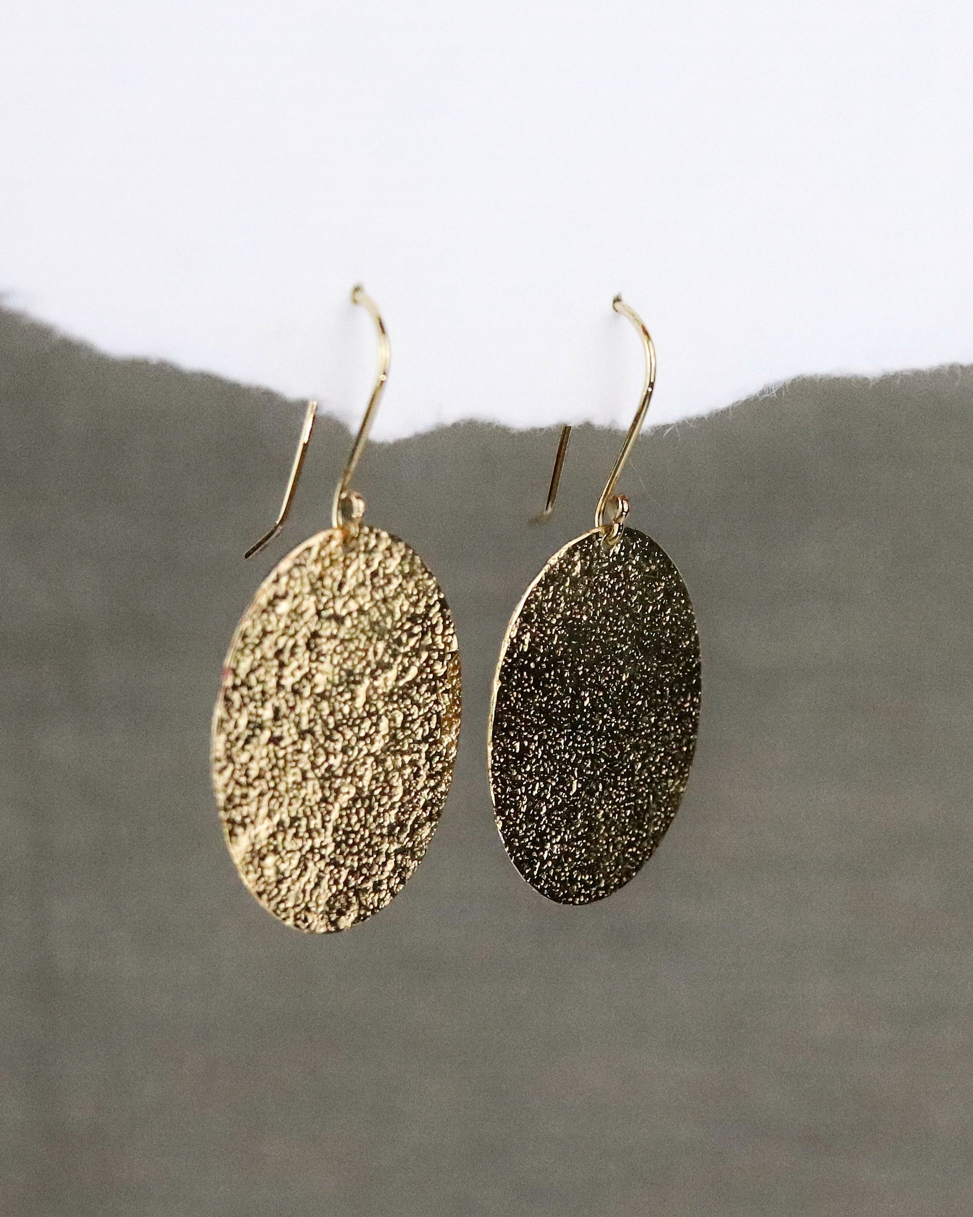 Boucles d'oreilles dormeuses Emery en vermeil (argent 925/1000 plaqué or 5 microns) sur fond papier blanc et tissus kaki vue de trois quarts
