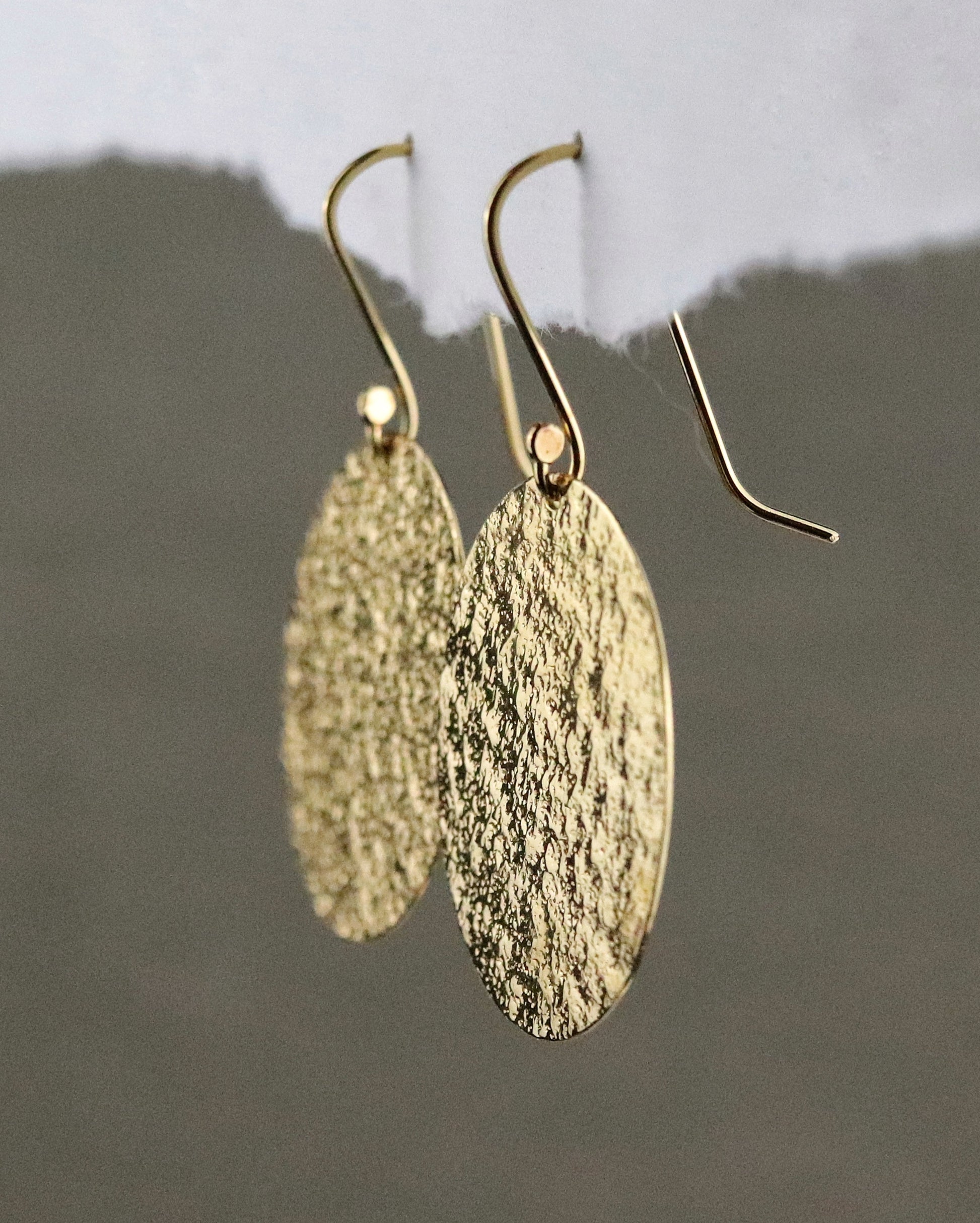 Boucles d'oreilles dormeuses Emery en vermeil (argent 925/1000 plaqué or 5 microns) sur fond papier blanc et tissus kaki vue de trois quarts