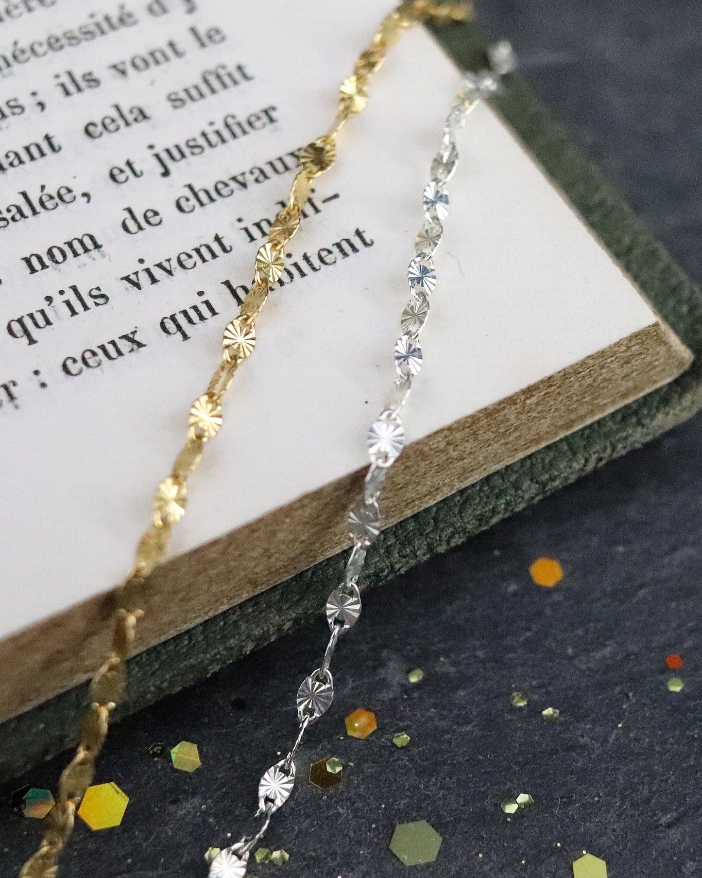 Bracelets Chaine soleil en argent 925/1000 et vermeil posés sur un livre et sur une ardoise naturelle