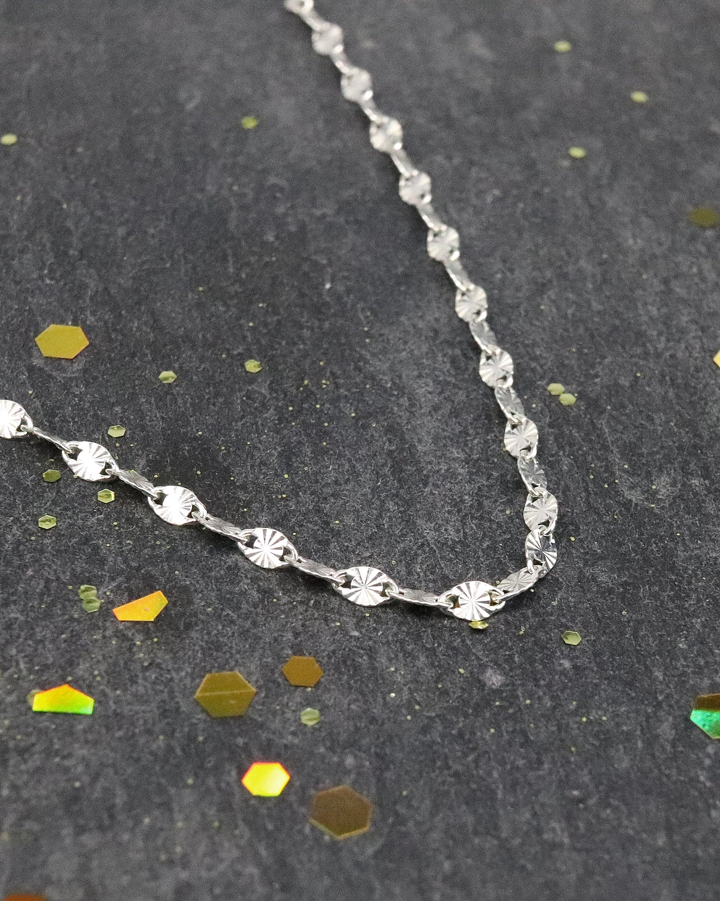 Chaine soleil argent zoom sur la maille, posée sur une ardoise naturelle