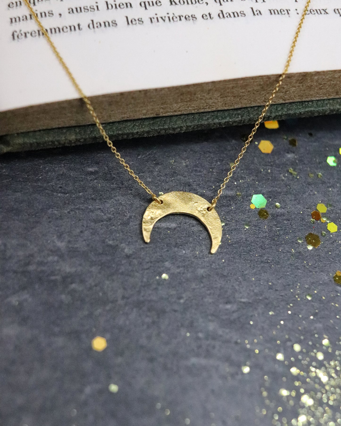 Collier pour femme Moon en vermeil (argent 925/1000 plaqué or 5 microns) posé sur un livre sur fond ardoise naturelle