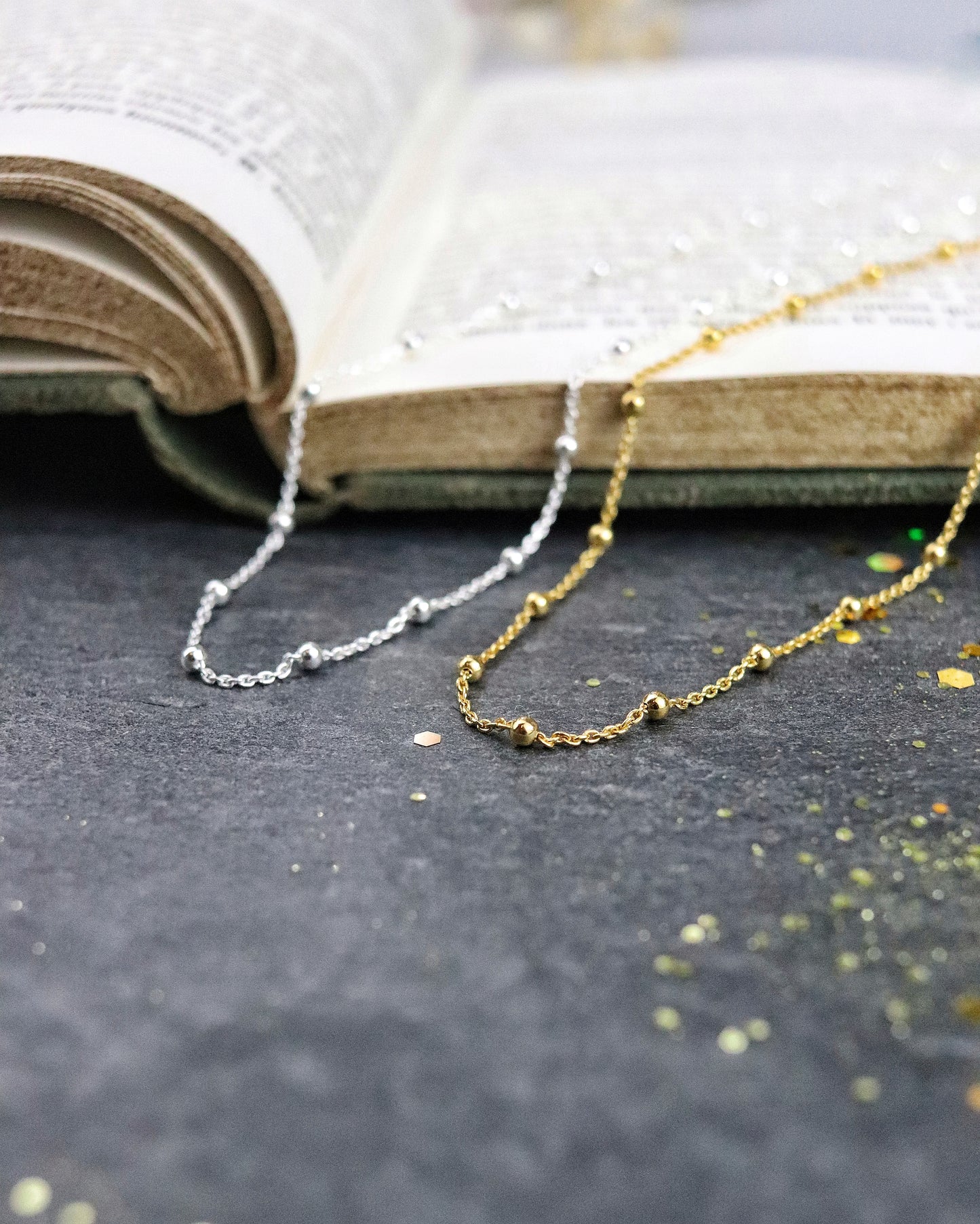 Colliers chaine boules en argent 925 et en vermeil posés sur un livre et une ardoise naturelle