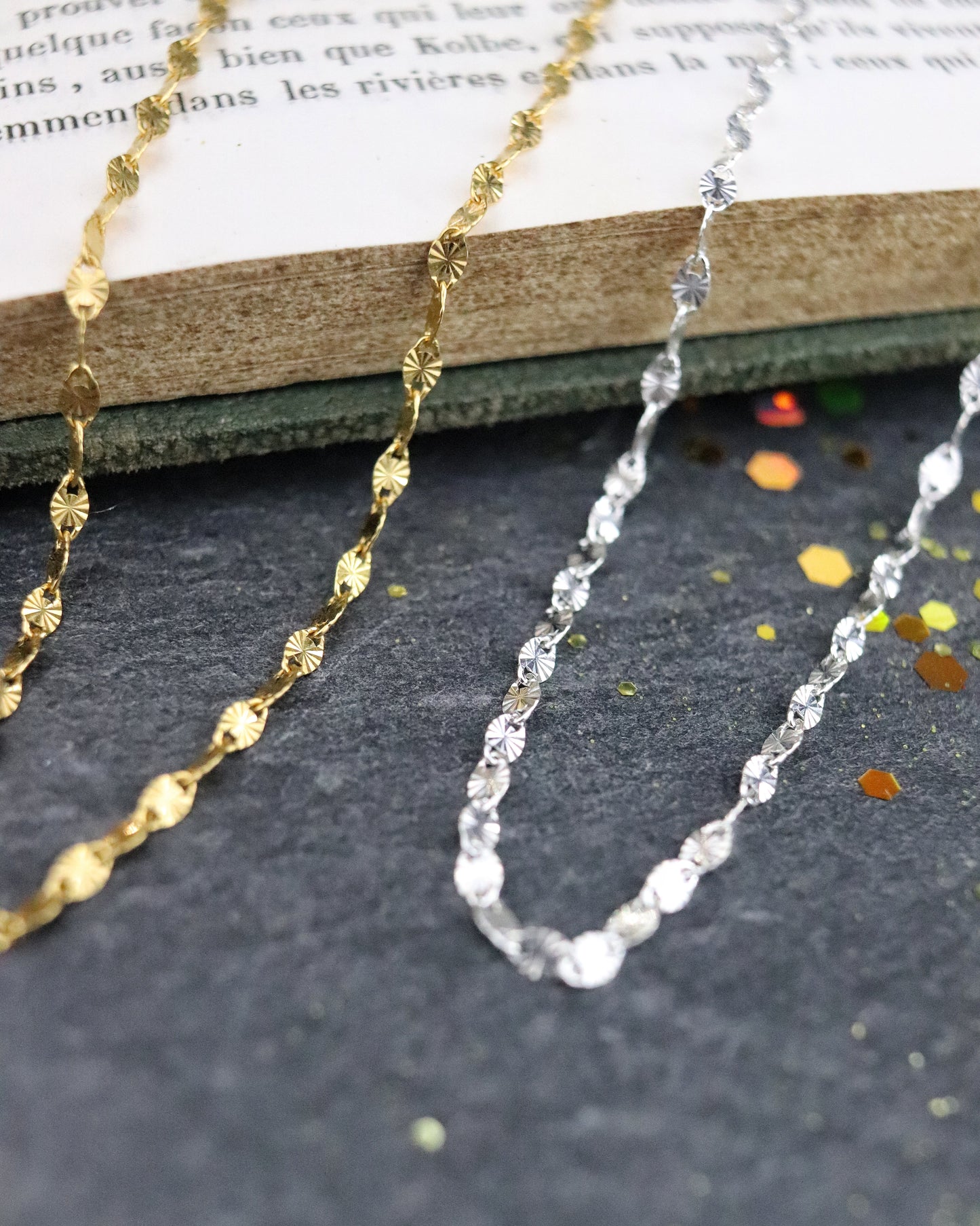 Colliers chaine Soleil en argent 925/1000 et vermeil posés sur un livre sur fond ardoise naturelle