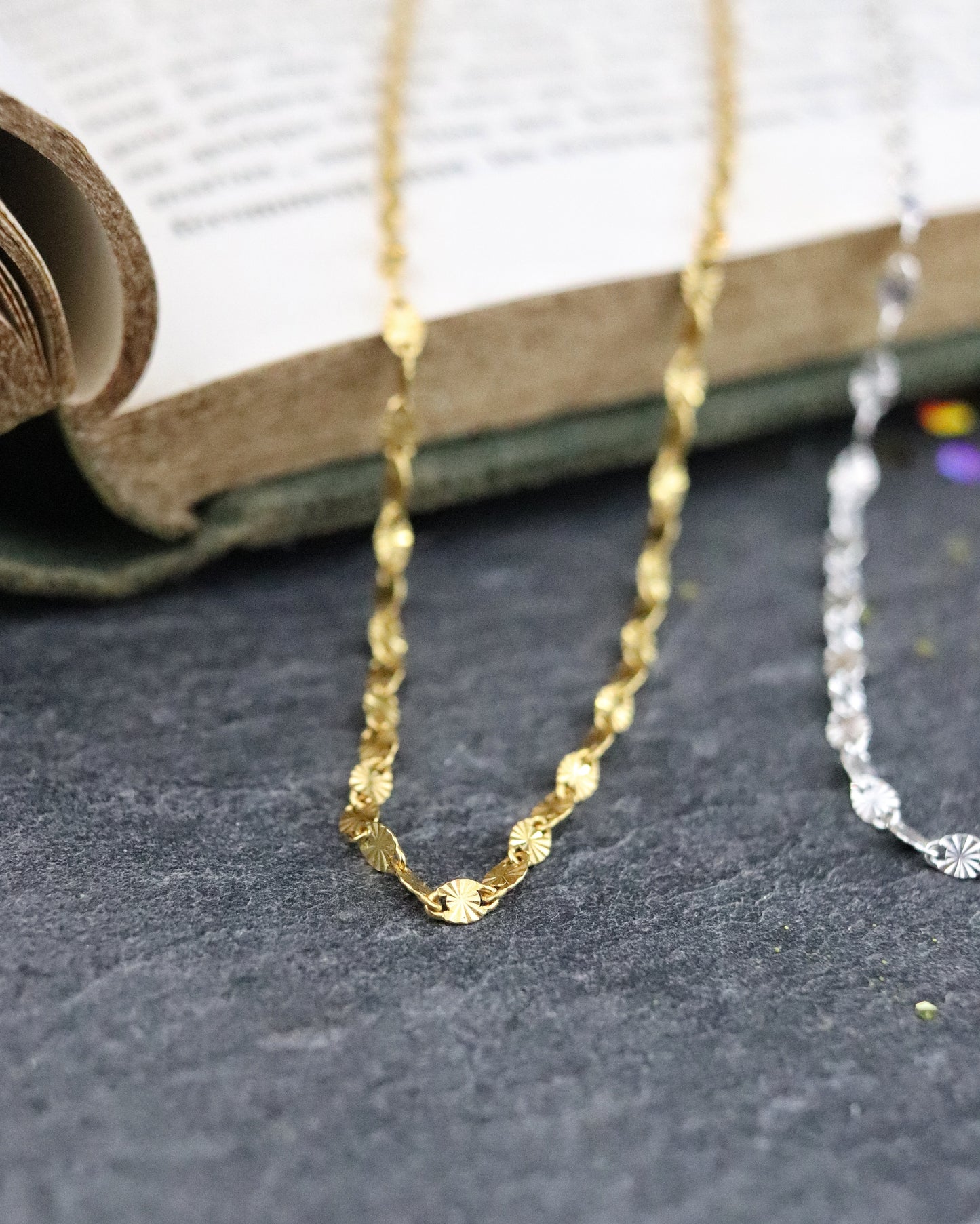 Colliers chaine Soleil en argent 925/1000 et vermeil posés sur un livre sur fond ardoise naturelle