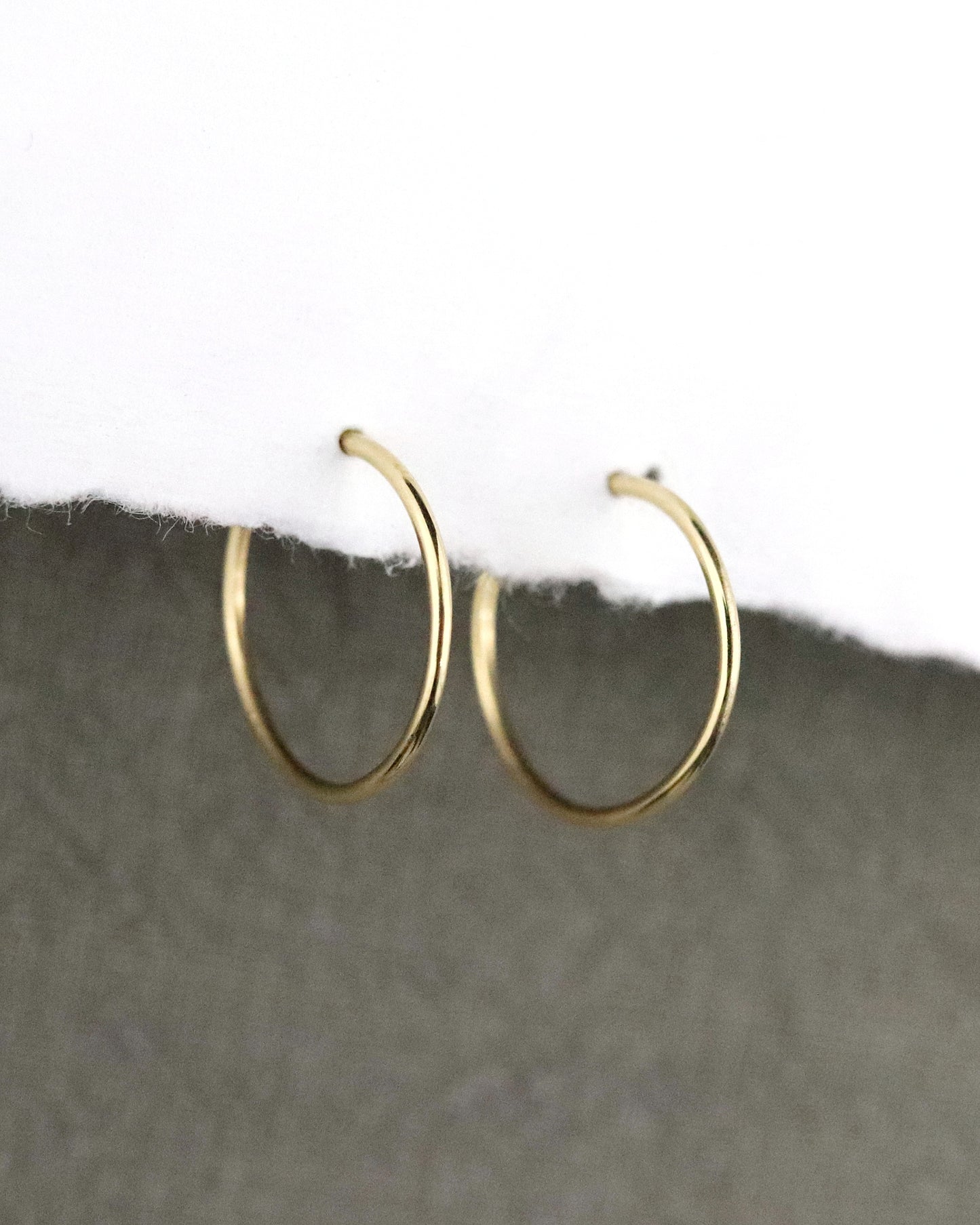 Créoles fines Boucles d'oreilles en or 750/1000 18k lisses sur papier blanc et fond tissus kaki