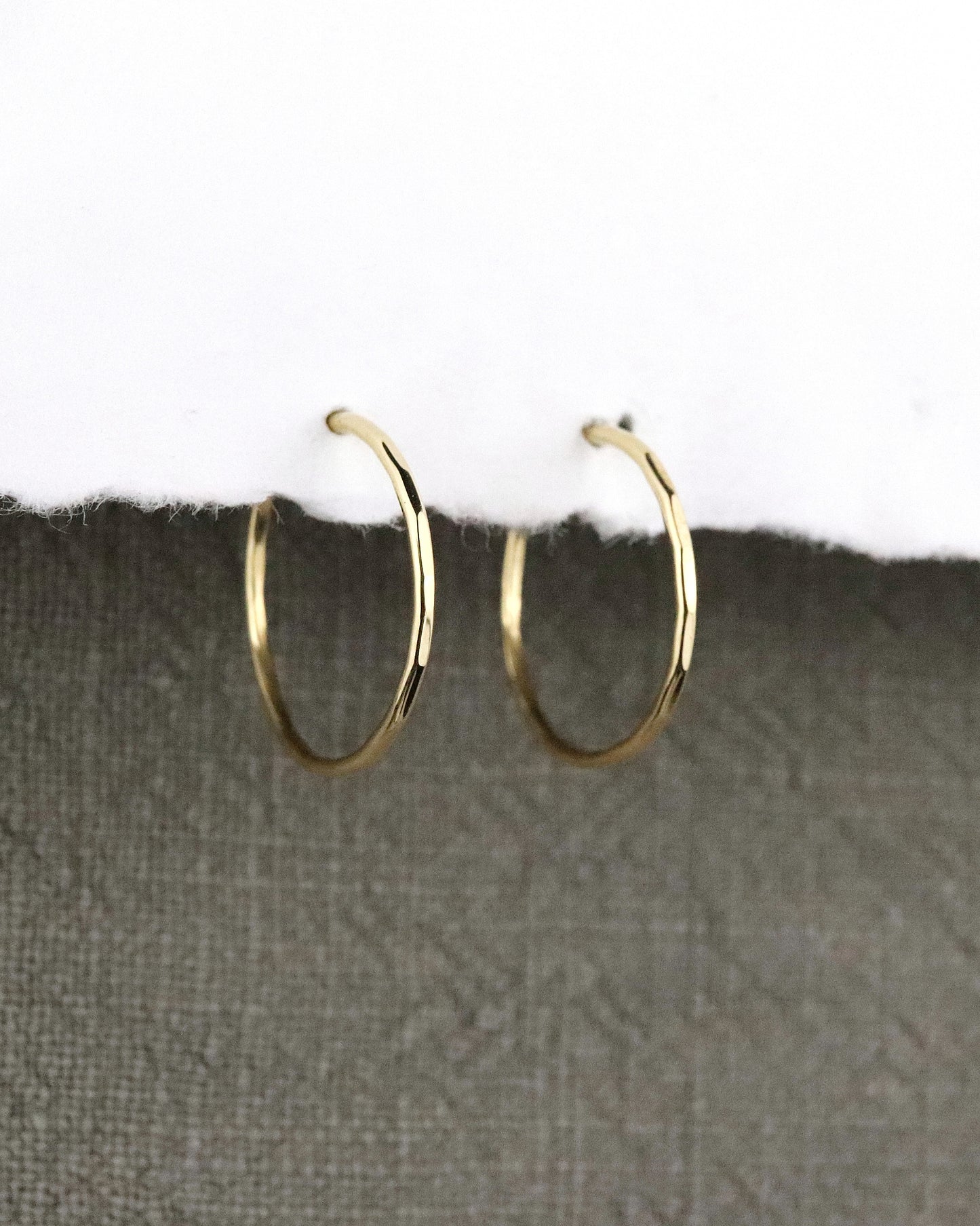 Créoles fines Boucles d'oreilles en or 750/1000 18k martelées sur papier blanc et fond tissus kaki
