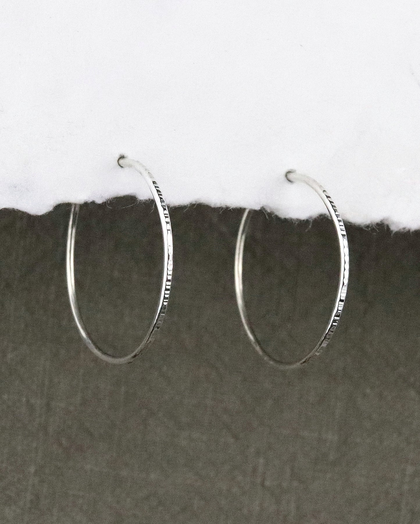boules d'oreilles créoles fines en argent 925/1000 taille M ciselées sur papier blanc et fond tissu kaki