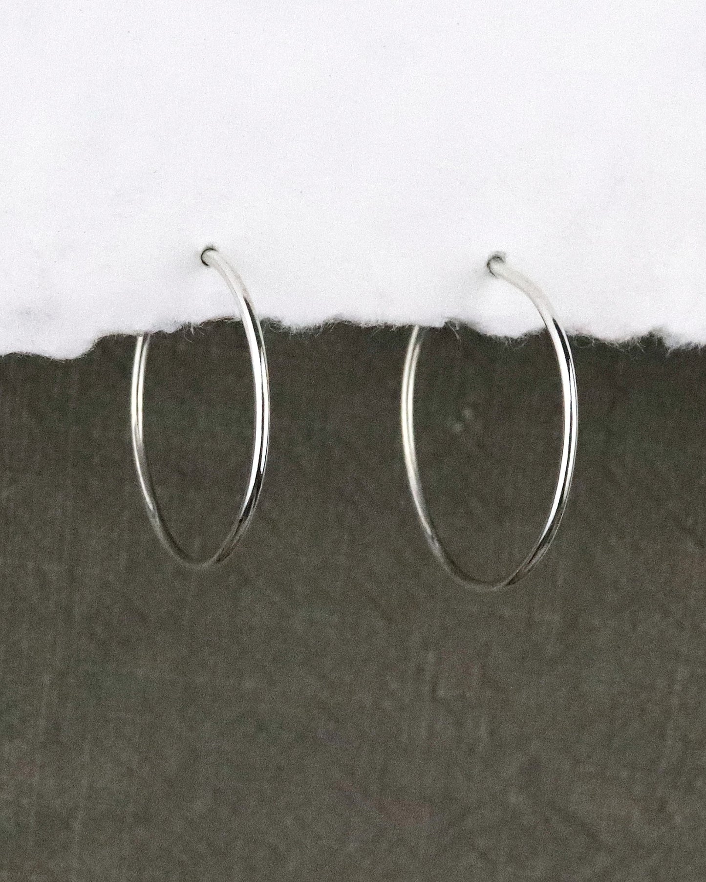 boules d'oreilles créoles fines en argent 925/1000 taille M lisses sur papier blanc et fond tissu kaki