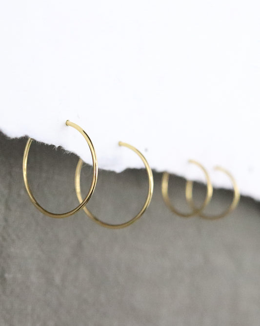 Boucles d'oreilles Créoles en or jaune 750 millièmes lisses fines sur un support en papier blanc et fond vert kaki Marion Chappaz