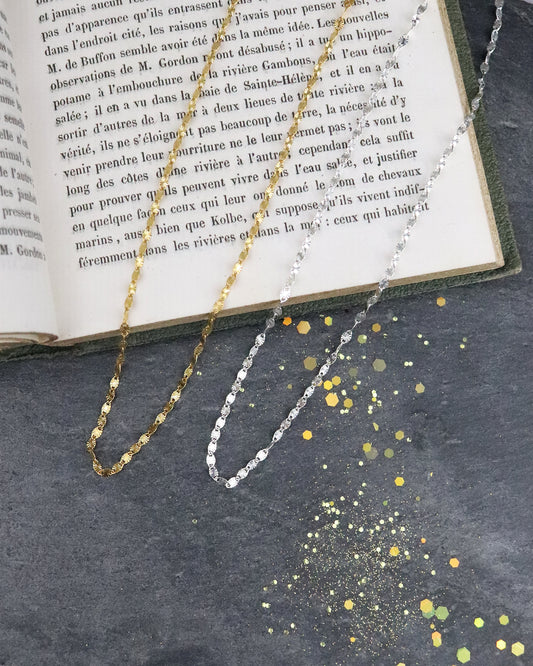 Colliers chaine Soleil en argent 925/1000 et vermeil posés sur un livre sur fond ardoise naturelle